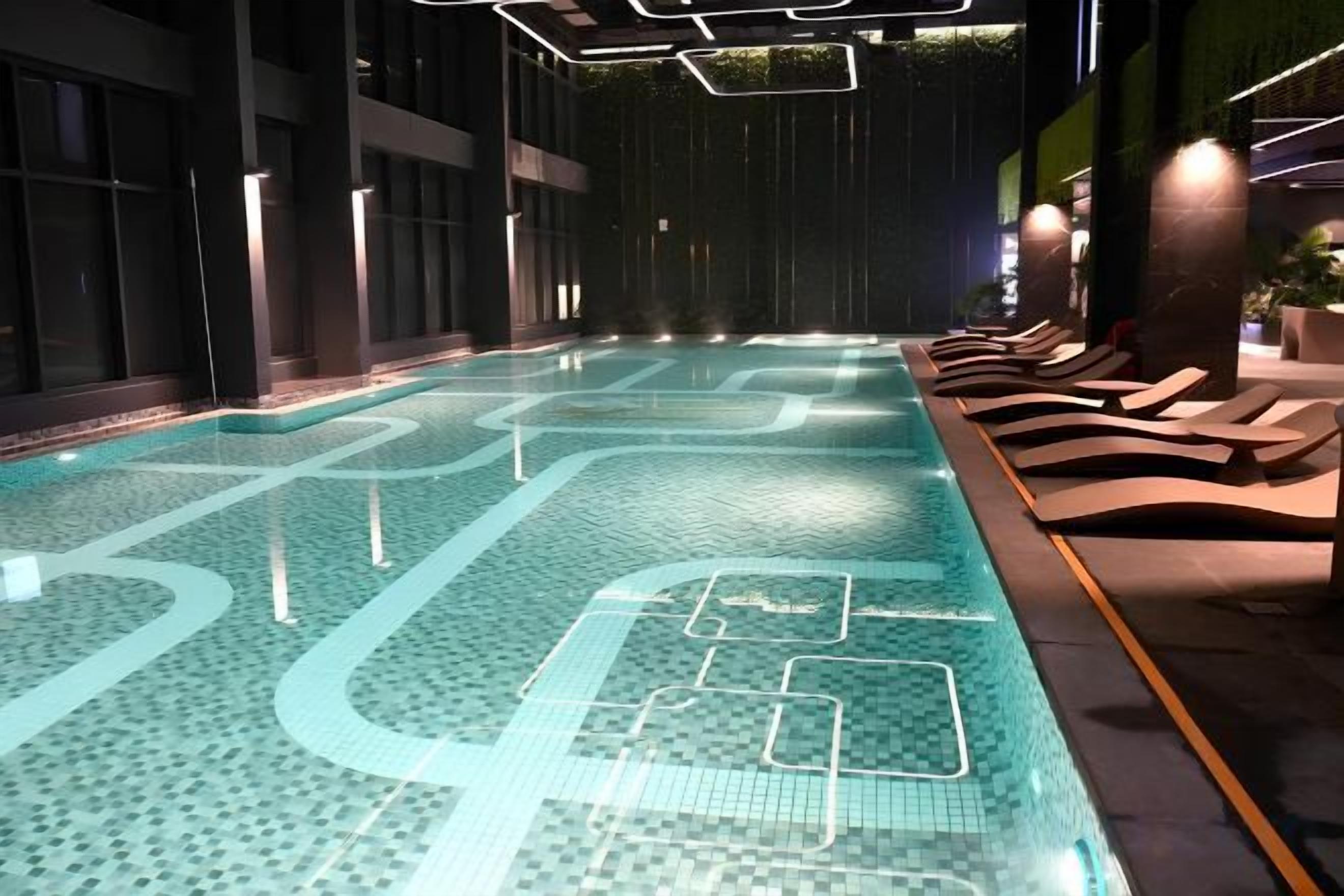 An indoor swimming pool with a tiled floor, lounge chairs, and a dark interior.