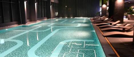 Une piscine intérieure avec un sol carrelé, des chaises longues et un intérieur aux couleurs sombres.
