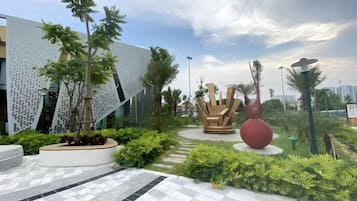 Un edificio moderno con fachada geométrica, una escultura central y un jardín ajardinado.