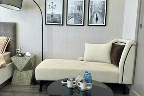 A modern hotel room with a sofa, a coffee table with drinks, and framed pictures on the wall.