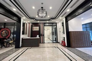 A hotel lobby with a reception desk, a chandelier, and a patterned floor.