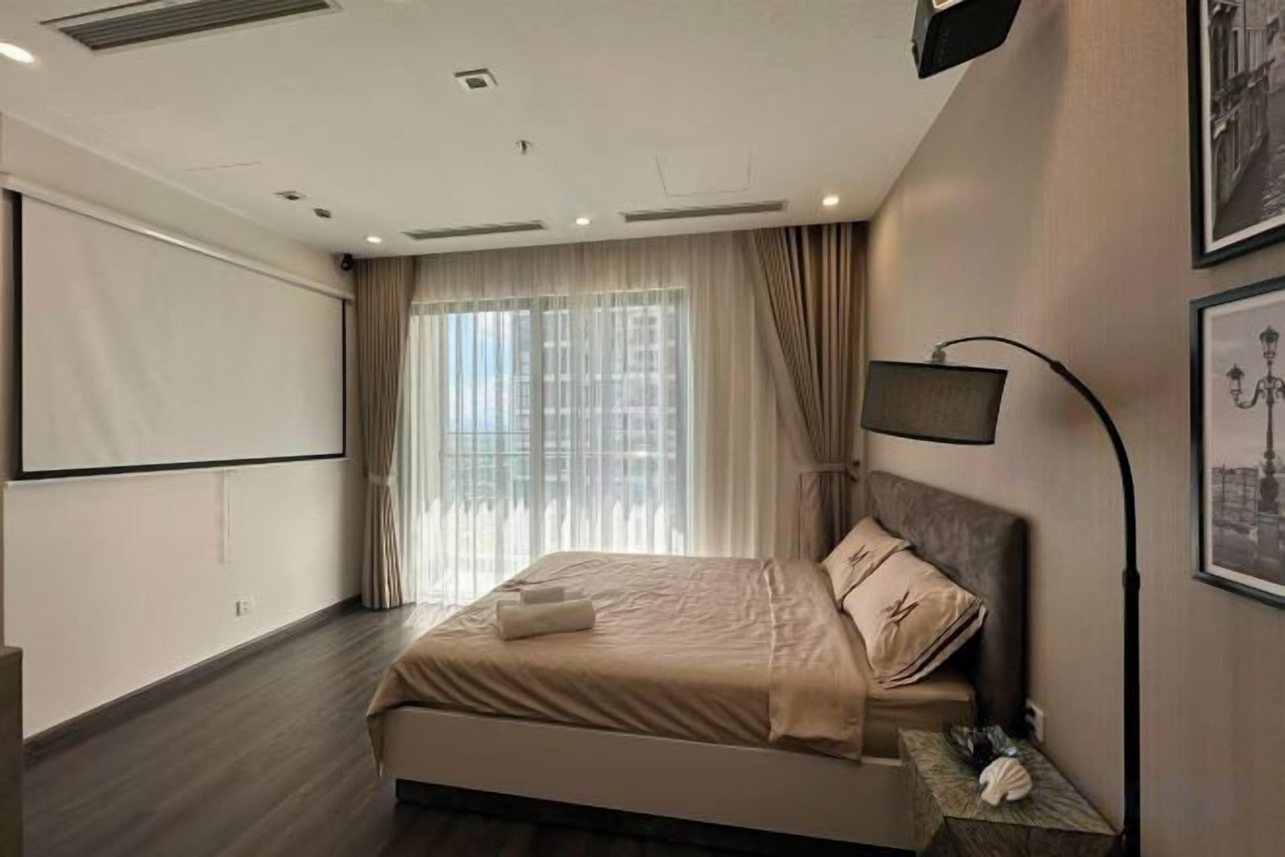 A hotel room with a bed, a projector screen, a lamp, and a window with curtains.