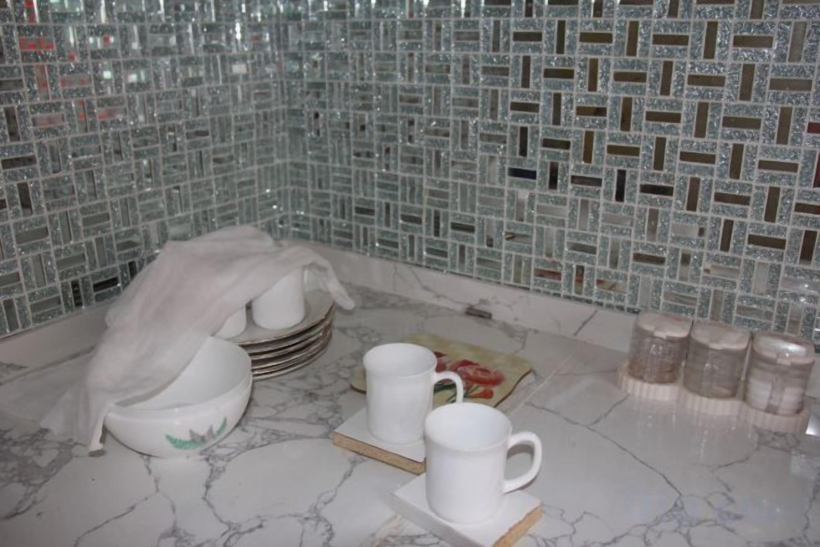 A bathroom with a tiled mosaic wall, a stack of white bowls, a white mug, and a set of salt and pepper shakers.