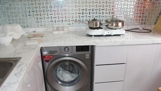 Cocina compacta con lavadora de acero inoxidable integrada, estufa pequeña y salpicadero de azulejos.