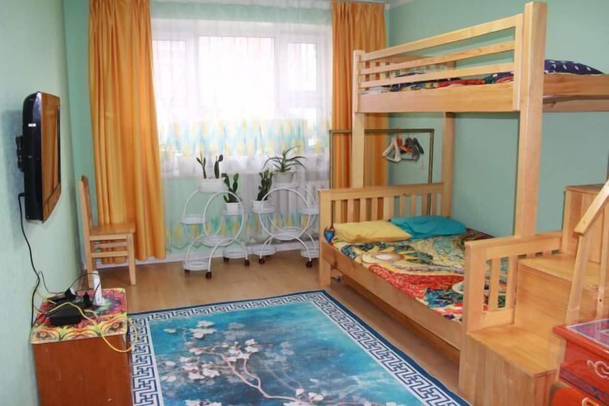 A bunk bed room with a desk, chair, and a window with curtains.
