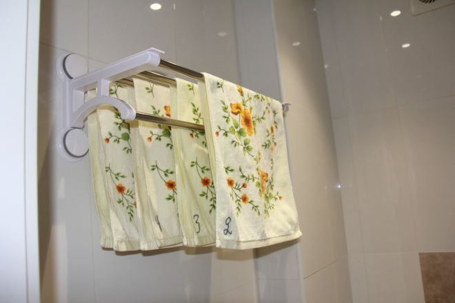 A bathroom with a white tiled wall, a white towel rack with floral towels, and a white shower curtain.
