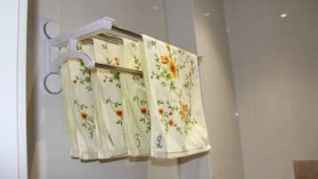 A bathroom with a white tiled wall, a white towel rack with floral towels, and a white shower curtain.