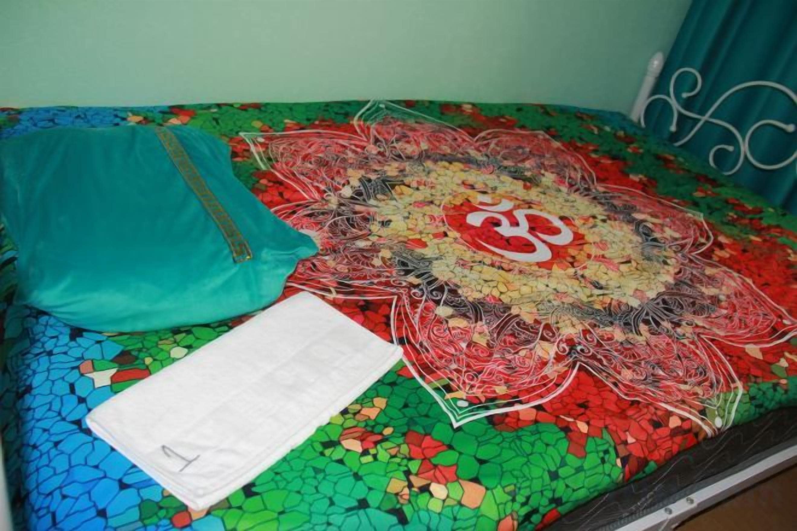 Una cama con un edredón colorido, una almohada azul turquesa y una almohada blanca.