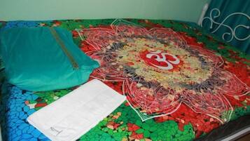 Una cama con un edredón colorido, una almohada azul turquesa y una almohada blanca.