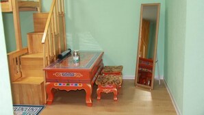 Una habitación con una escalera de madera, una mesa con cubierta de vidrio y base roja, y un taburete pequeño.