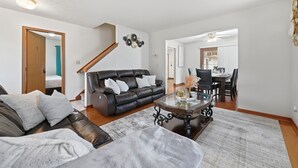 Un salon moderne avec un canapé en cuir, une table basse en verre et un coin repas comprenant une table et des chaises en bois.