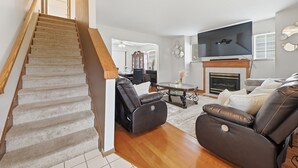 Un escalier mène à un salon doté d’une cheminée, de canapés en cuir et d’un téléviseur à écran plat.