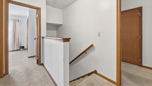 Un couloir doté d’un sol recouvert de moquette, d’une porte en bois et d’un escalier avec une rampe en bois.