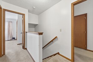 A hallway with a carpeted floor, a wooden door, and a staircase with a wooden handrail. - 3BR Cozy&Peaceful Retreat +small gym (Cleveland)