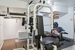 A gym with various exercise equipment, including a bench press, weight racks, and a squat rack. - 3BR Cozy&Peaceful Retreat +small gym (Cleveland)