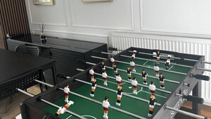 A foosball table in a room with white walls, two framed artworks, and a radiator.