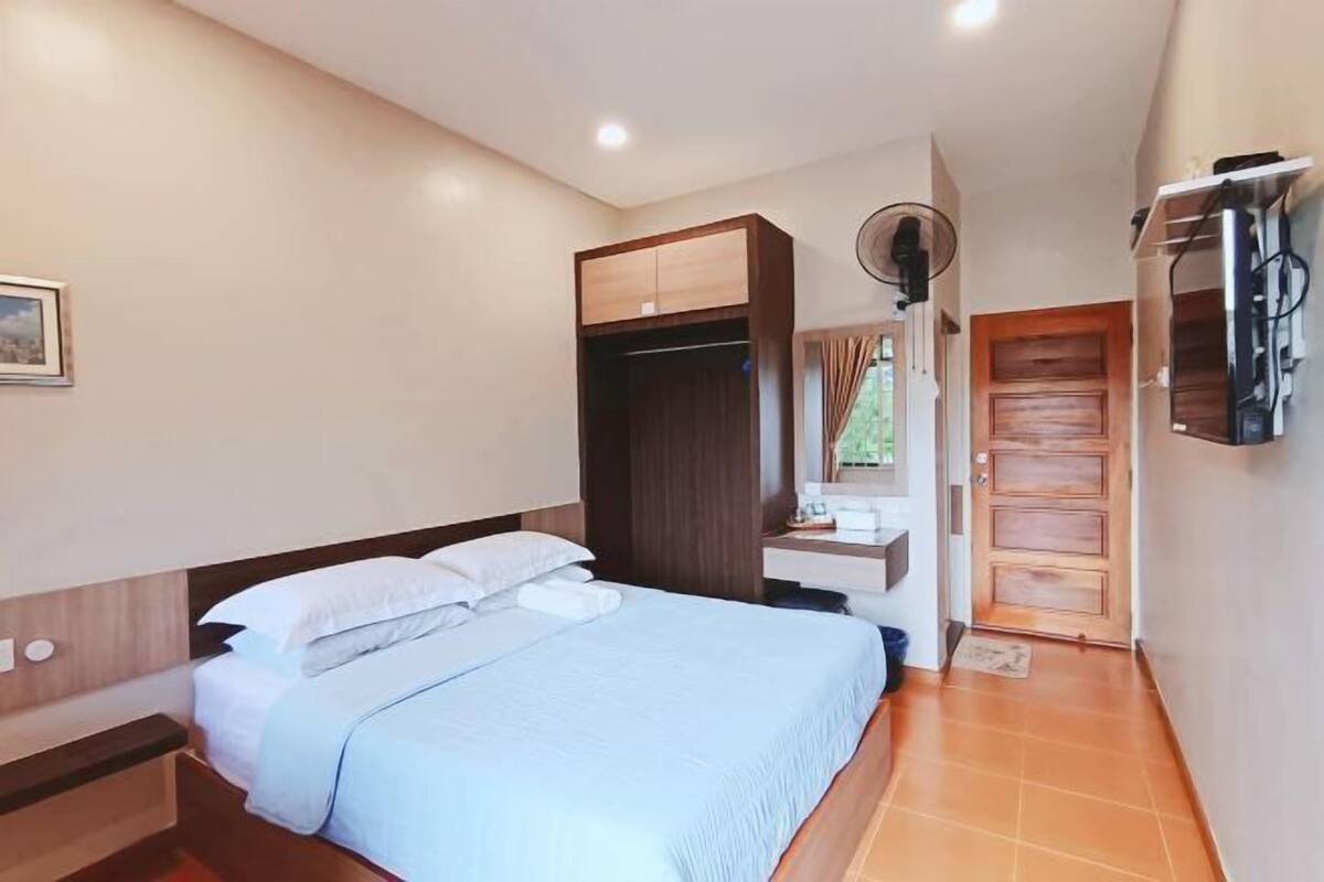 A bedroom with a bed, a wardrobe, a mirror, a TV mounted on the wall, and a door leading to another room.