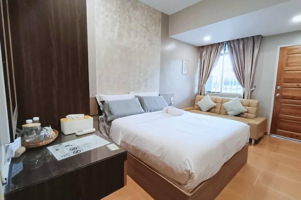 A hotel room with a large bed, a bedside table with a lamp, a sofa, and a window with curtains.