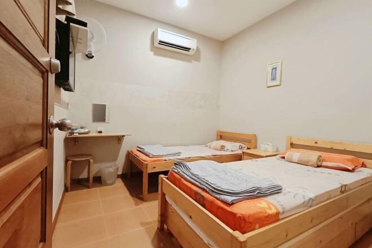 A small, tidy room with two wooden beds, a desk, and a chair.