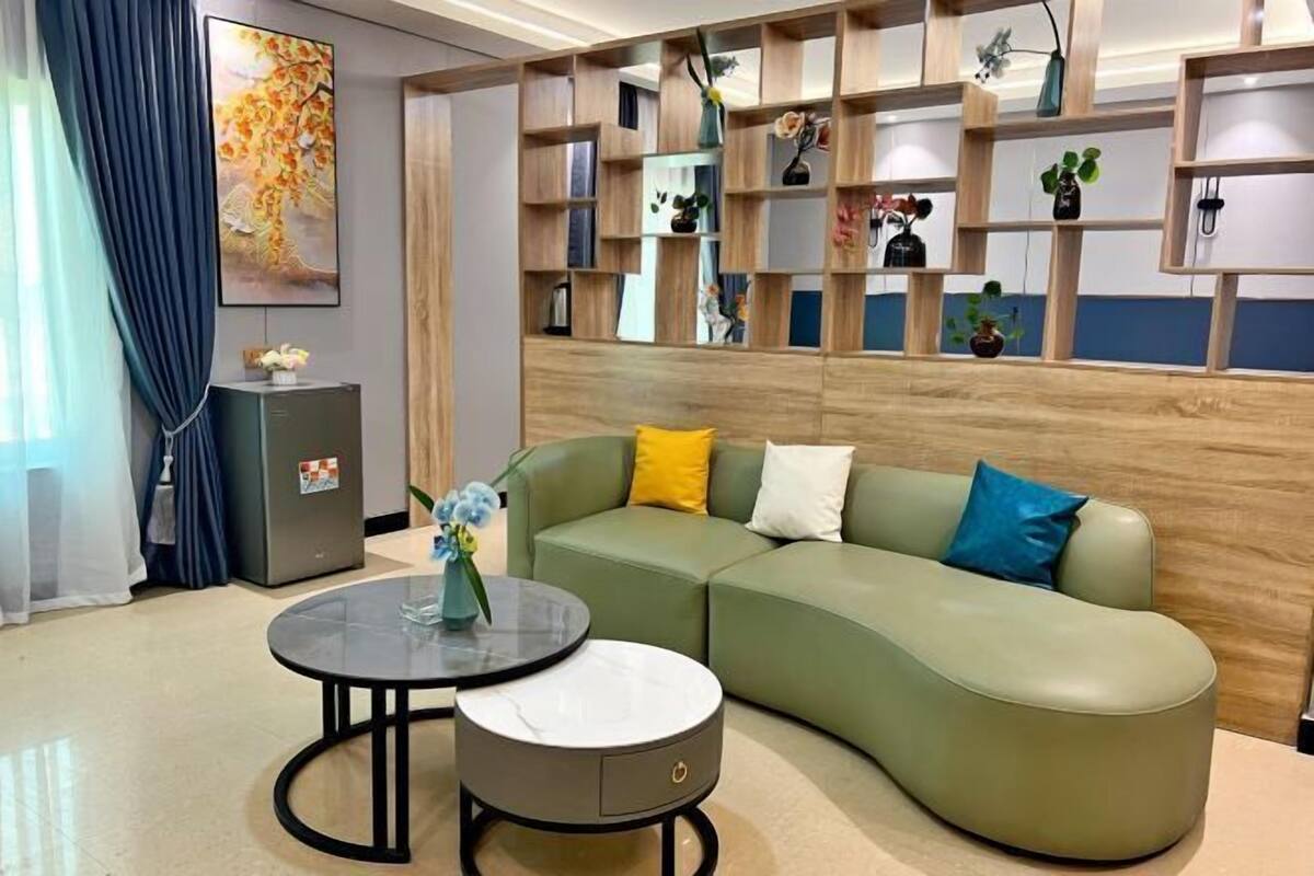 A modern living room with a green sectional sofa, a round coffee table, and a built-in wooden shelving unit with various decorative items.