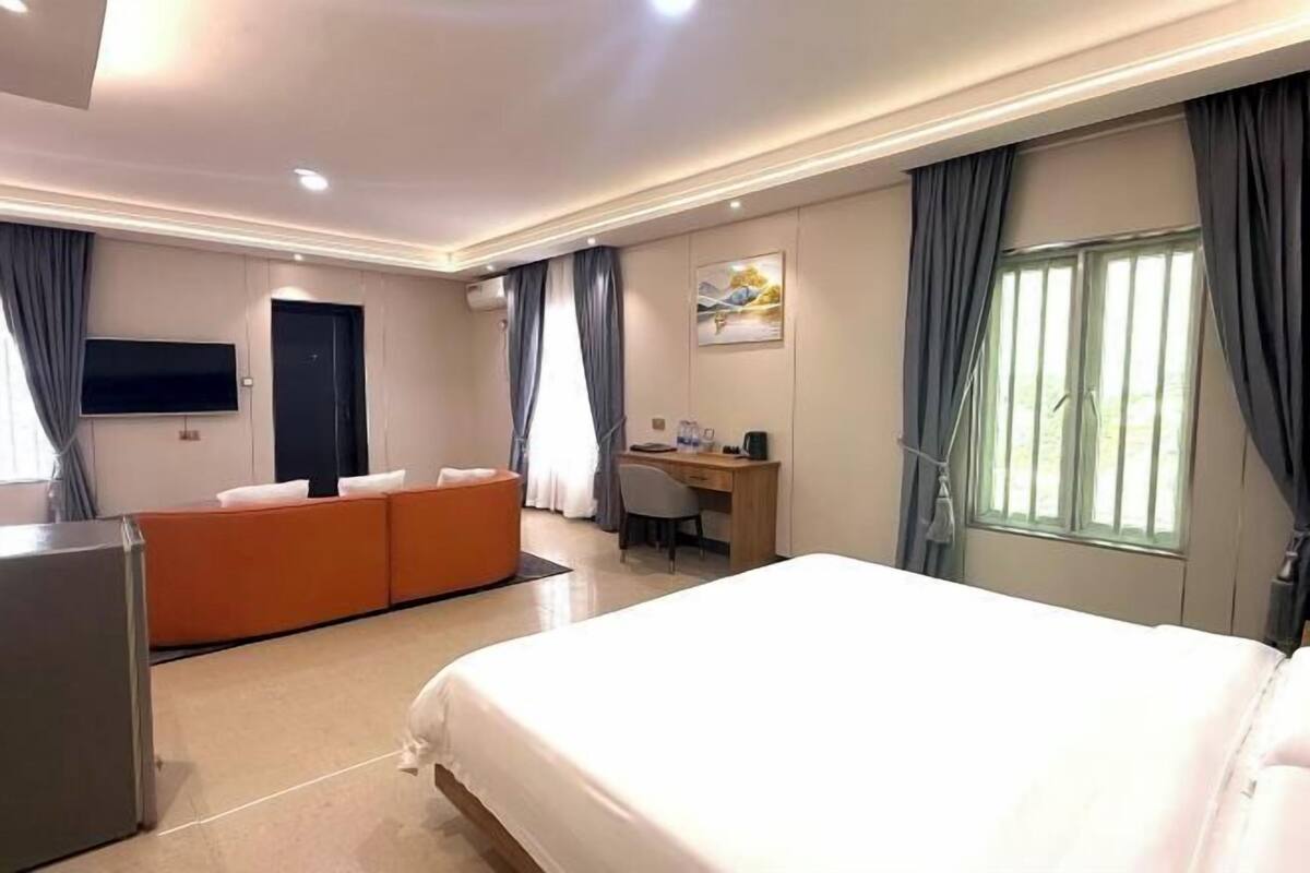 A hotel room with a large bed, a desk, a sofa, and a TV.