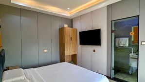 A bedroom with a bed, a wooden wardrobe, a TV, and a glass door leading to a bathroom. - TDH HOTEL (Ikeja)