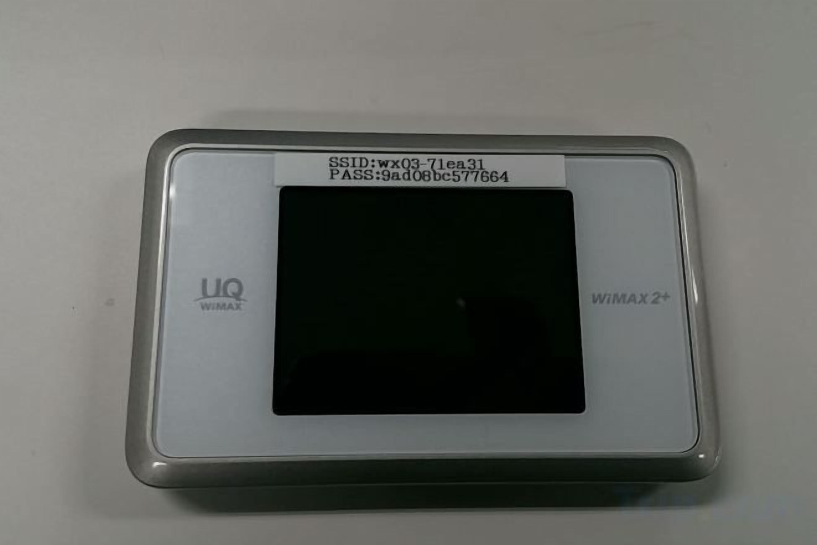 Ein UQ WIMAX2+ Gerät mit schwarzem Bildschirm, das SSID und PASS Informationen anzeigt.