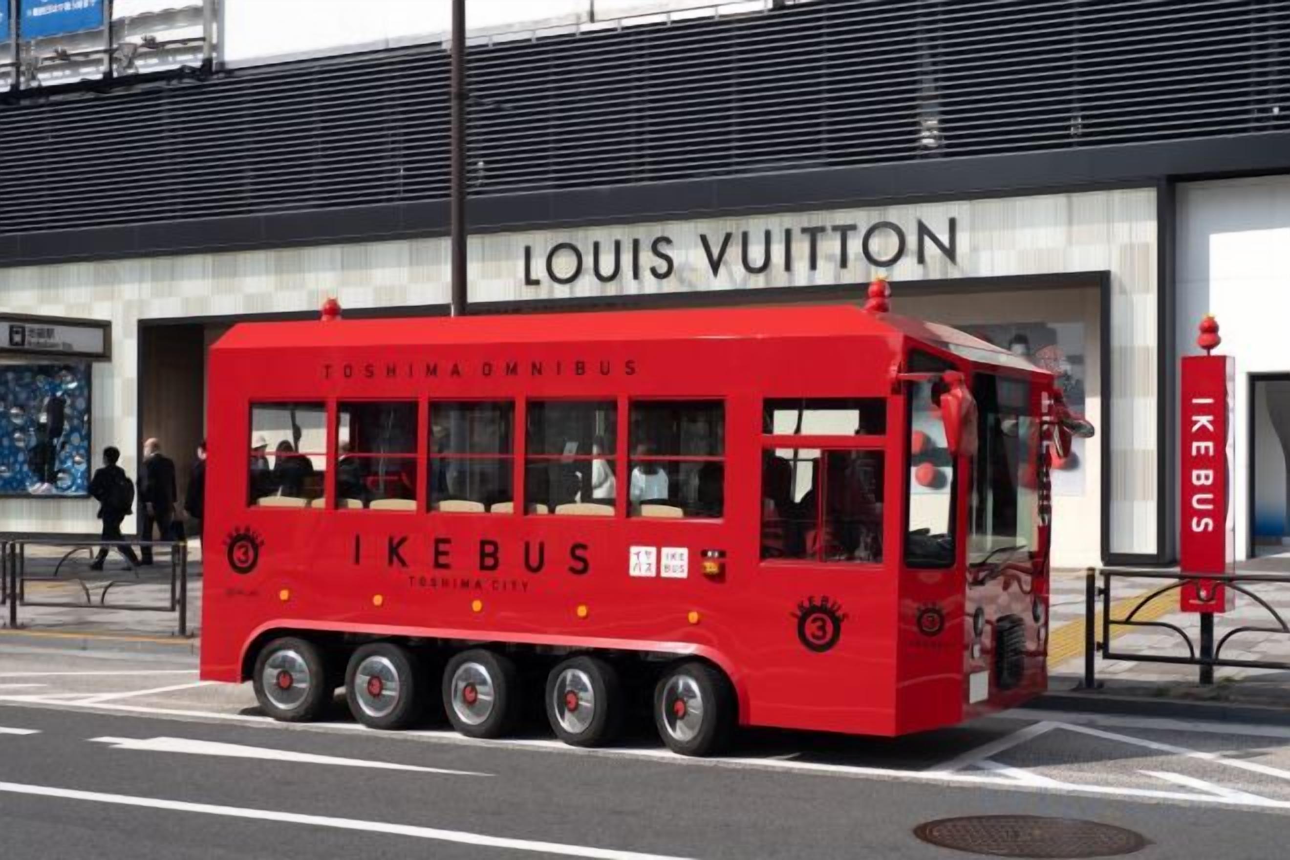 A red IKEBUS with 'TOSHIMA OMNIBUS' and 'IKEBUS' branding parked in front of a Louis Vuitton store.