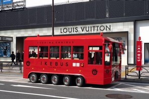 A red IKEBUS with 'TOSHIMA OMNIBUS' and 'IKEBUS' branding parked in front of a Louis Vuitton store. - Ikebukuro Central Hotel (Tokyo)