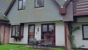 A two-story house with a brick facade, a tiled roof, and a small patio with a table and chairs.