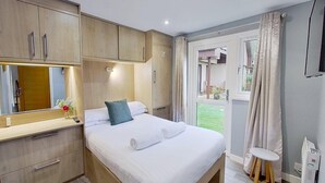 A bedroom with a bed, a mirror, a small table, and a window with curtains.