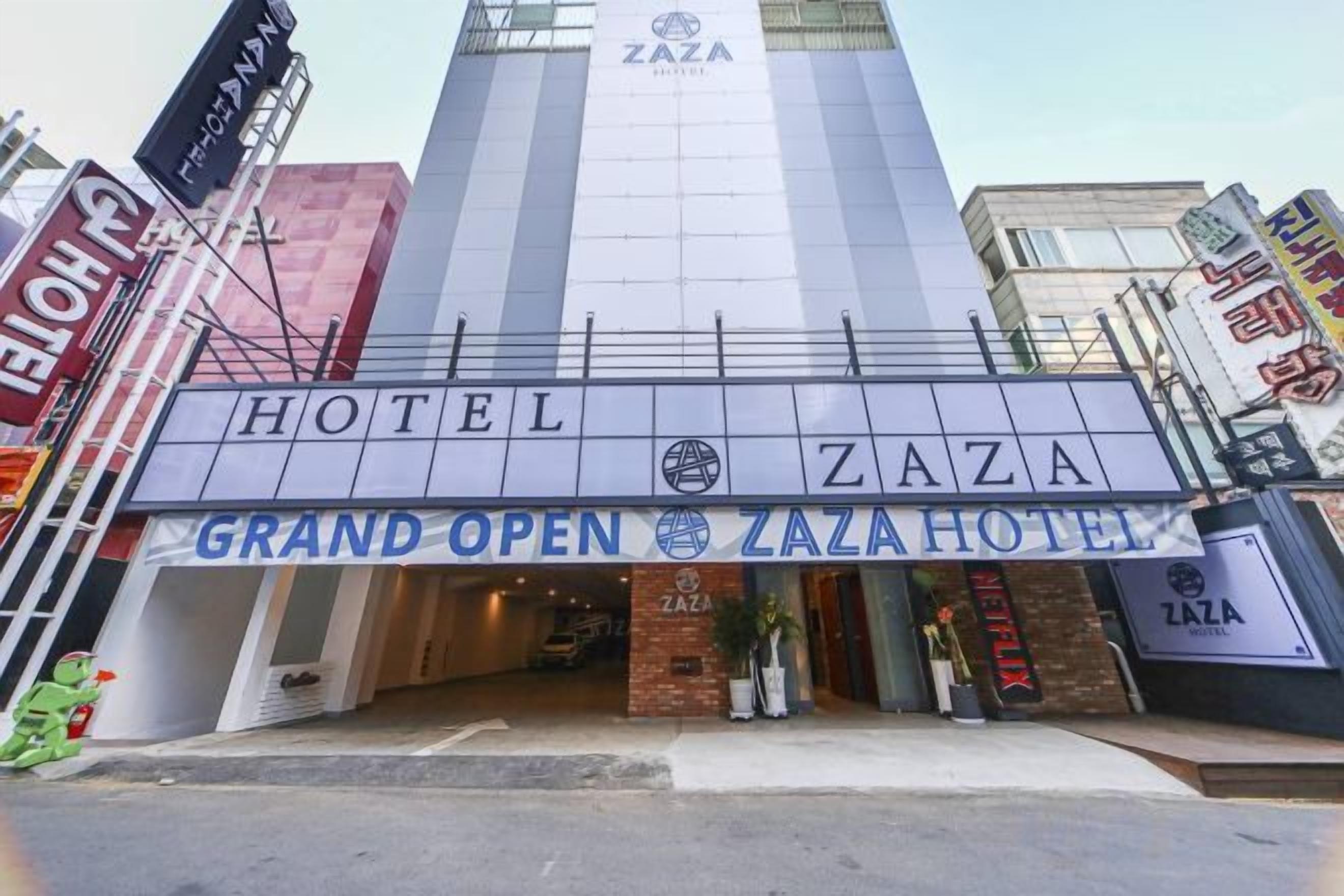 Een hotelentree met een opvallend bord waarop staat 'HOTEL ZAZA GRAND OPEN ZAZAHOTEL'.