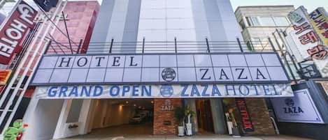 Entrada de un hotel con un letrero llamativo que dice 'HOTEL ZAZA GRAND OPEN ZAZAHOTEL'.