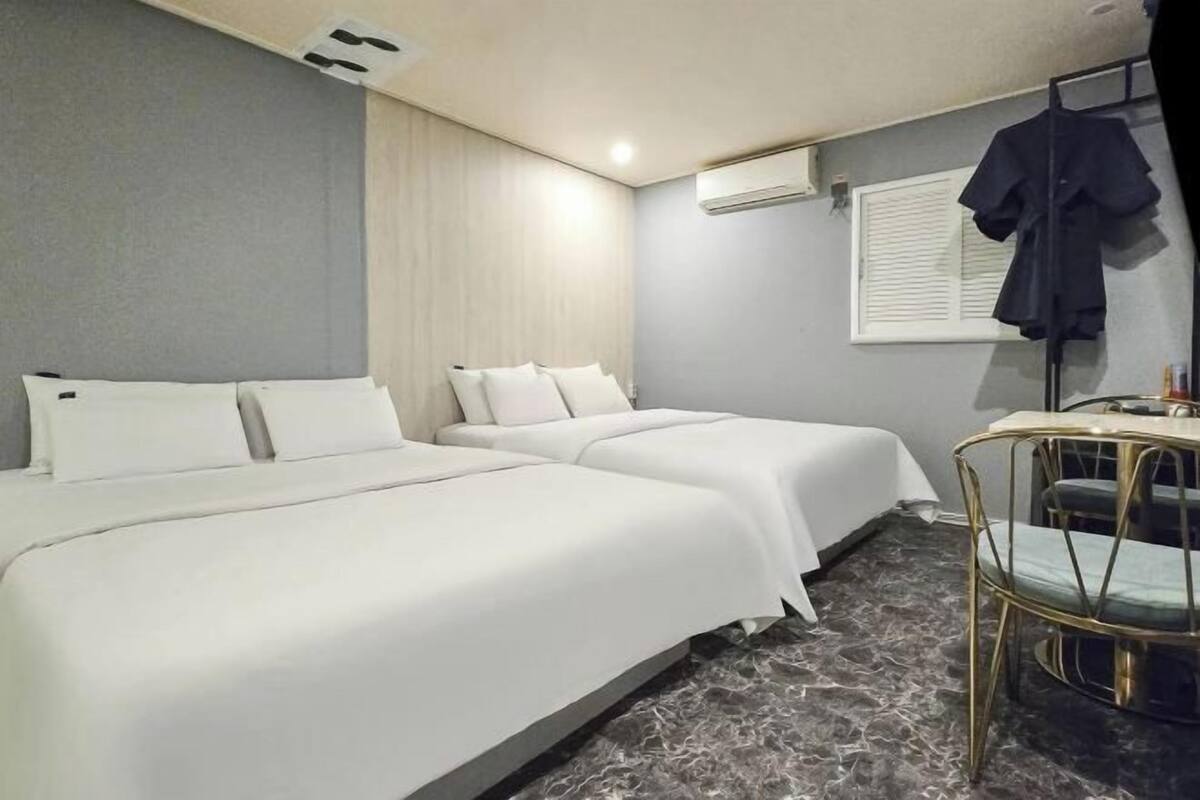 Habitación de hotel con dos camas, una silla, un equipo de aire acondicionado y una ventana con persianas.