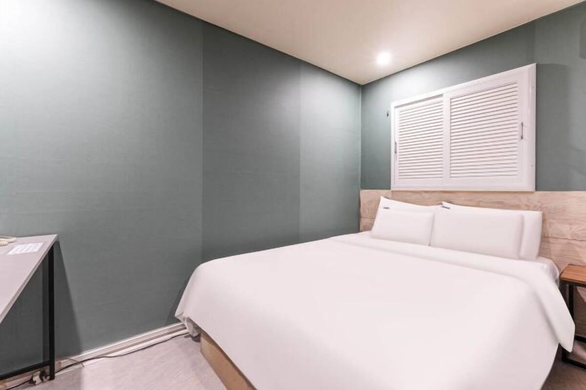 Un dormitorio con cama, escritorio y ventana con persianas.