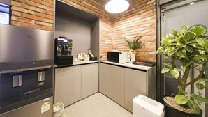 A compact kitchen with a brick wall, a coffee machine, a refrigerator, and a potted plant. - ZAZA Hotel (Bucheon-si)