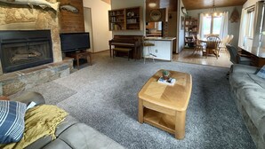 Una sala de estar acogedora con chimenea, televisor, piano y comedor con sillas y mesa.