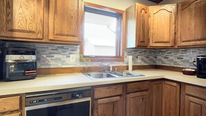 Una cocina con armarios de madera, lavavajillas, estufa y ventana con luz natural.