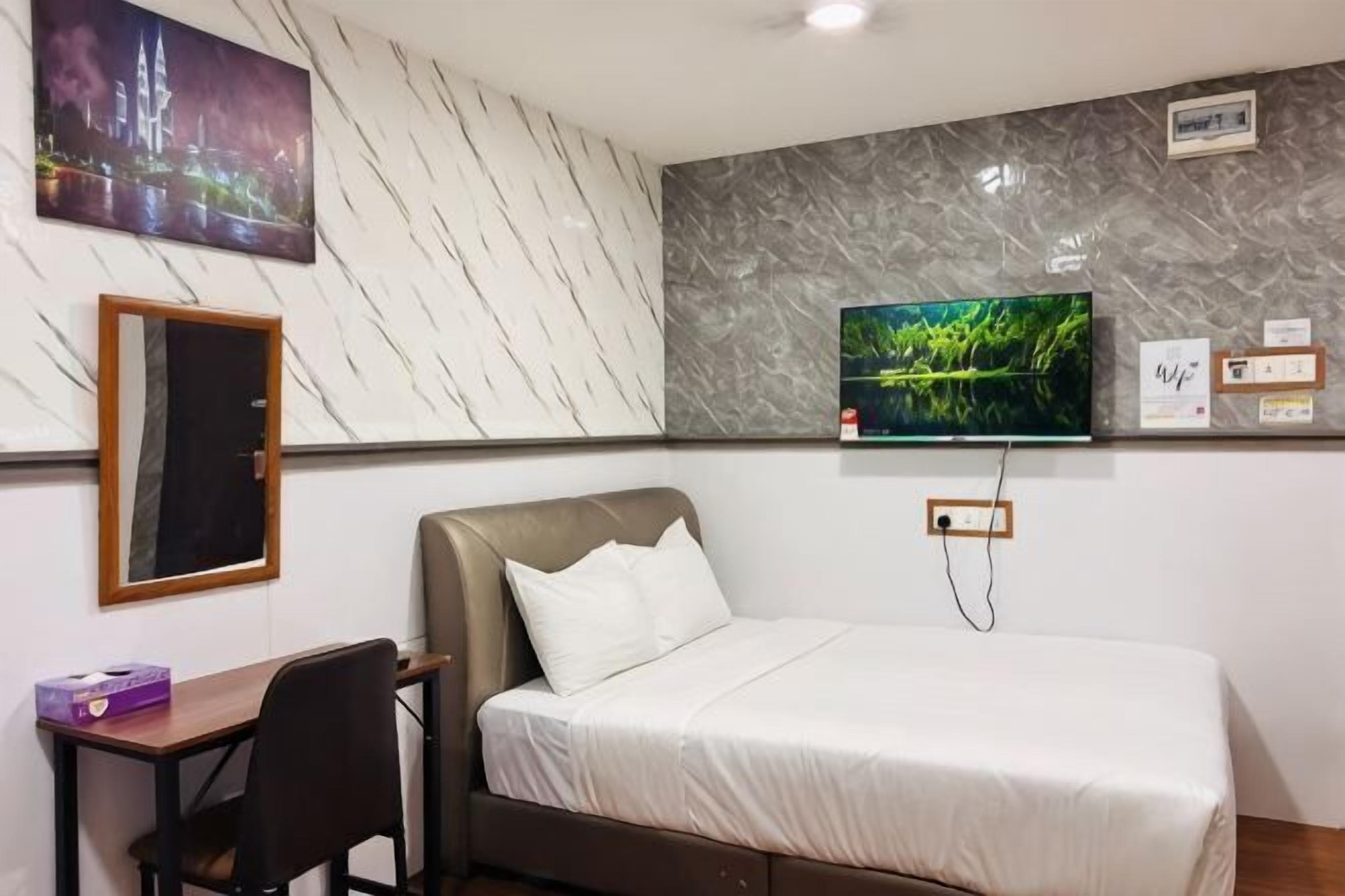 Ein Hotelzimmer mit einem Bett, einem Schreibtisch, einem Stuhl, einem an der Wand befestigten Fernseher und einem Gemälde.