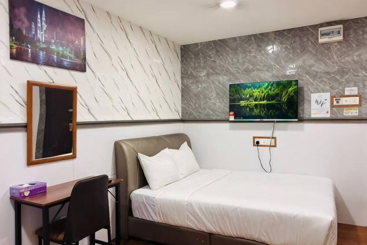 A hotel room with a bed, a desk, a chair, a television mounted on the wall, and a painting.