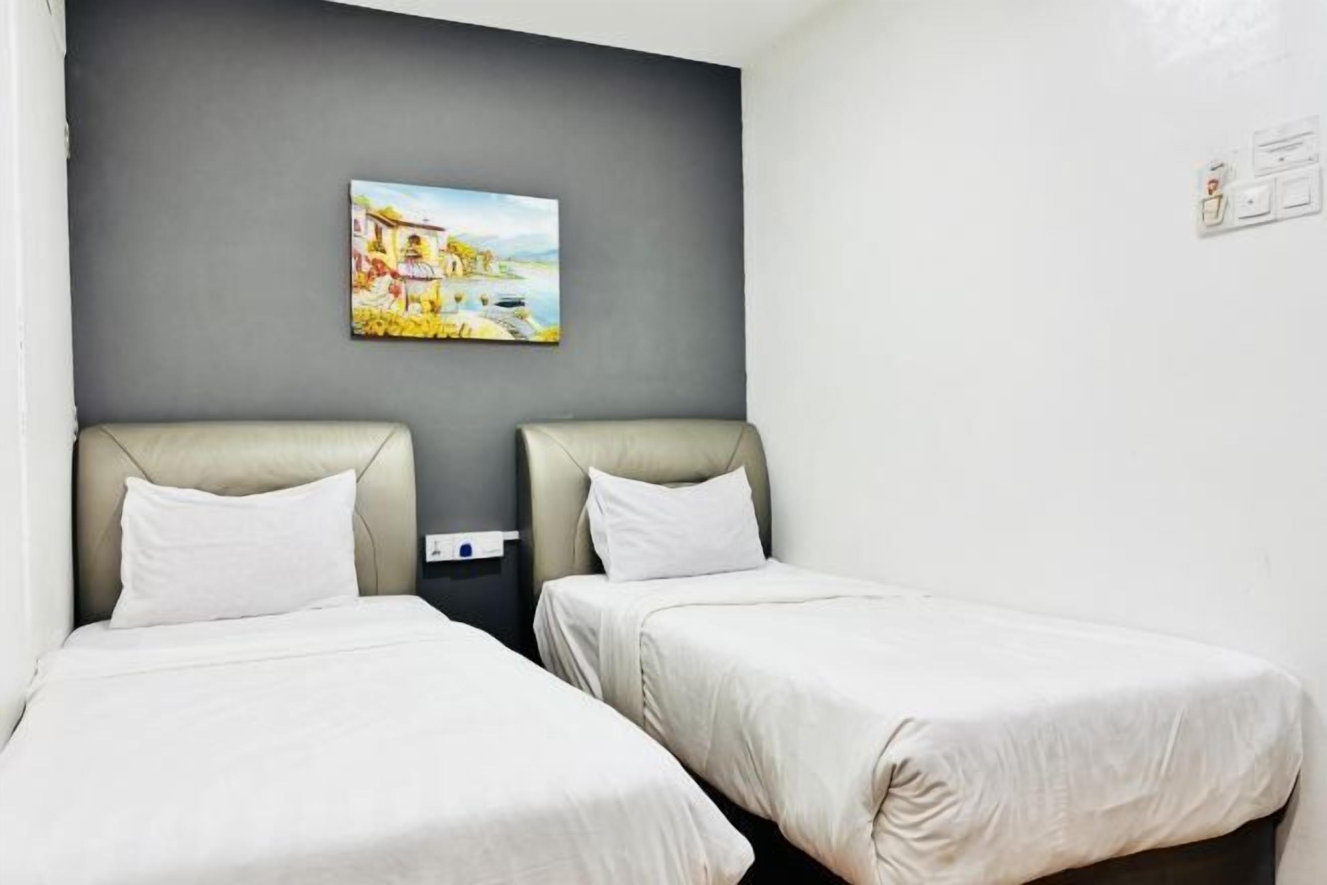 A hotel room with two single beds, a grey accent wall, and a painting above the beds.