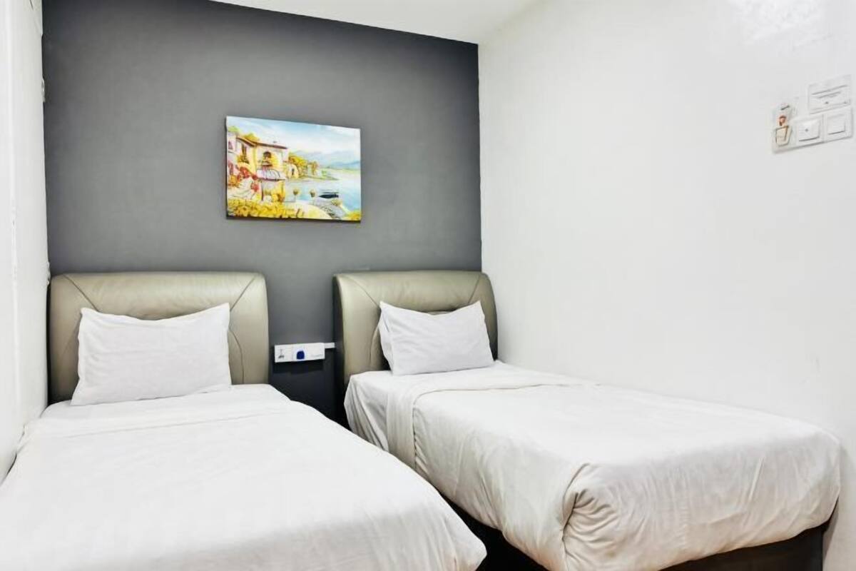 A hotel room with two single beds, a grey accent wall, and a painting above the beds.