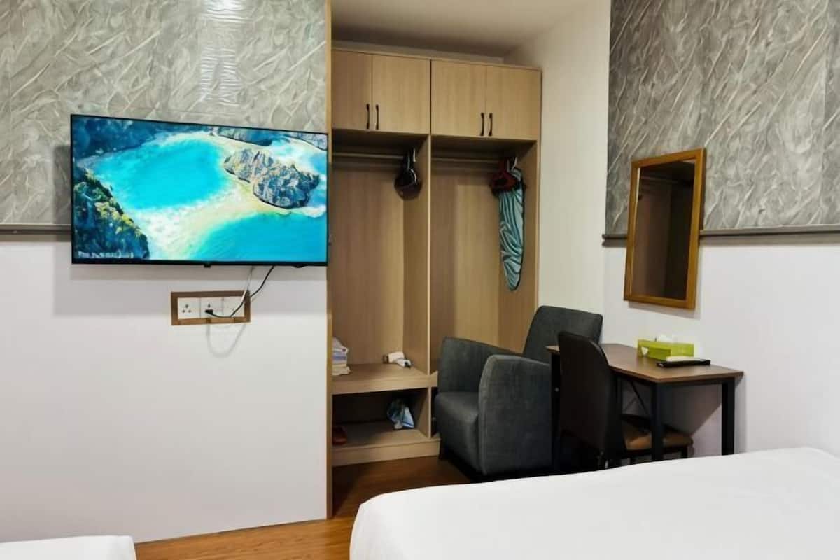 A hotel room with a bed, a desk, a chair, a television, a wardrobe, and a mirror.