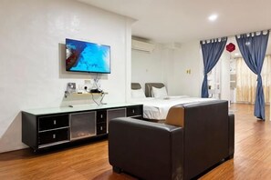 A modern hotel room with a flat-screen TV mounted on the wall, a bed with white linens, a black sofa, and a wooden floor. - Hotel Traveler's Majestic Retreat, Located in the Heart of Melaka (Melaka)