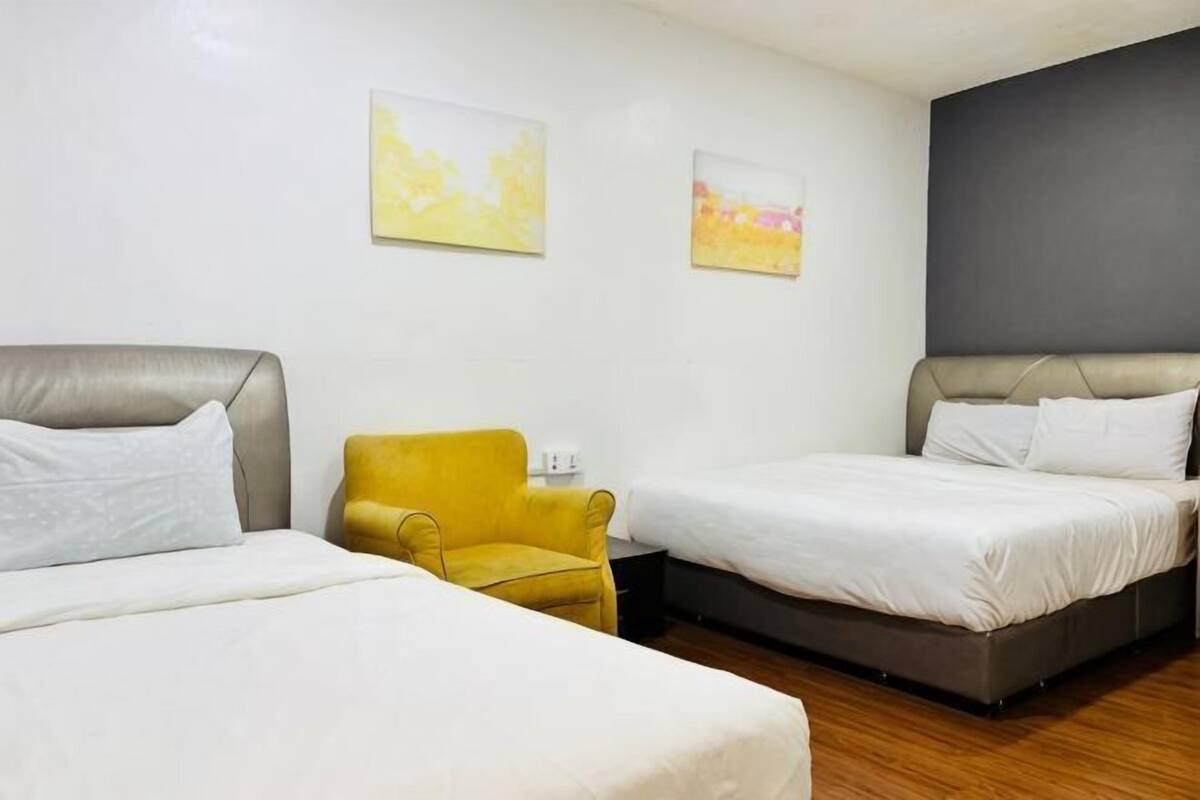 A hotel room with two beds, a yellow armchair, and two abstract paintings on the wall.