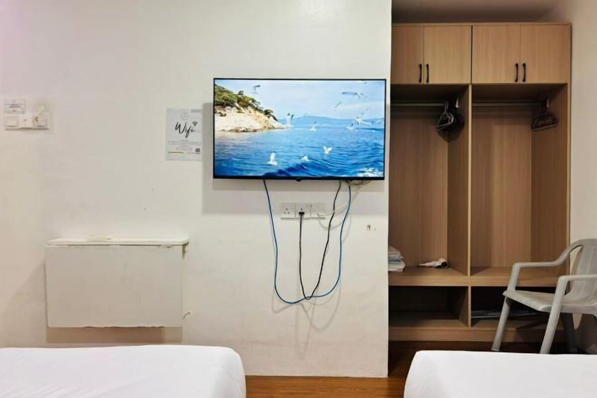 A room with a bed, a TV mounted on the wall displaying a scenic ocean view, a wooden wardrobe, and a white radiator.