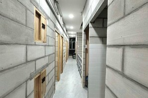 Un couloir avec un mur en béton d’un côté et un mur carrelé de l’autre, qui mène à un escalier.