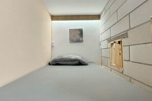 Een kleine kamer met een bed, een houten deur en een aan de muur hangend schilderij.