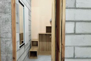 A narrow hallway with wooden steps leading to a door, a window on the left, and a brick wall on the right. - Tonbon Home - Japanese style living (Ho Chi Minh City)