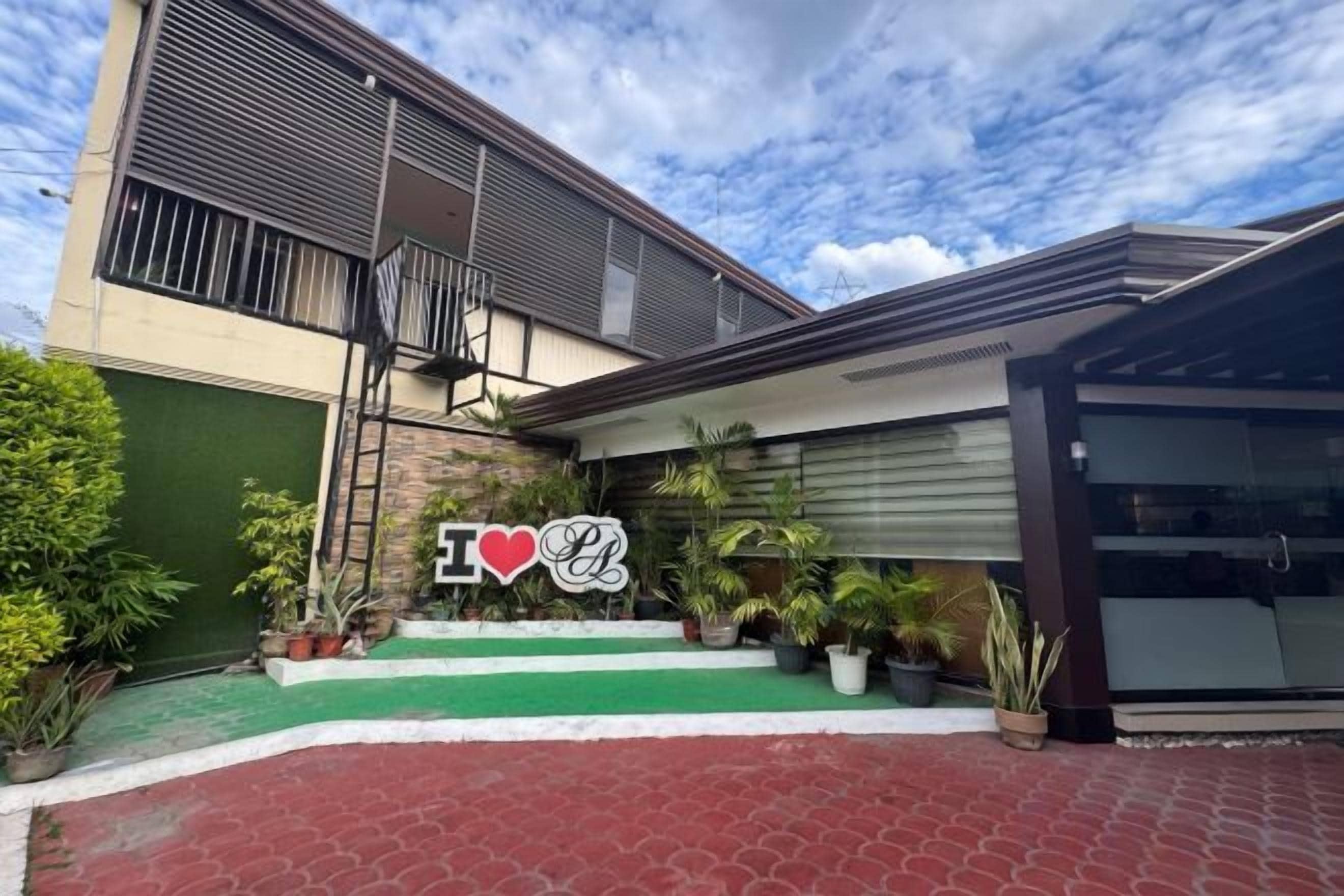 A modern house with a green front yard, a staircase leading to the entrance, and a sign with 'I ♥ L' on the front.